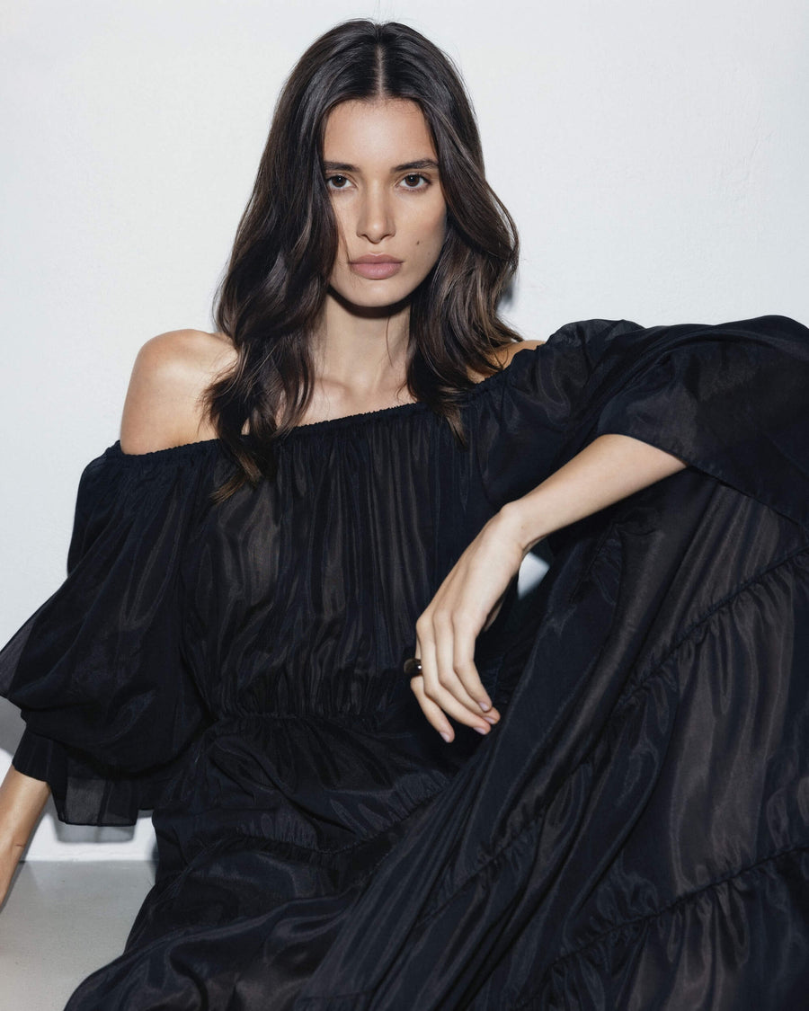 Woman wearing a black off-shoulder dress against a white background